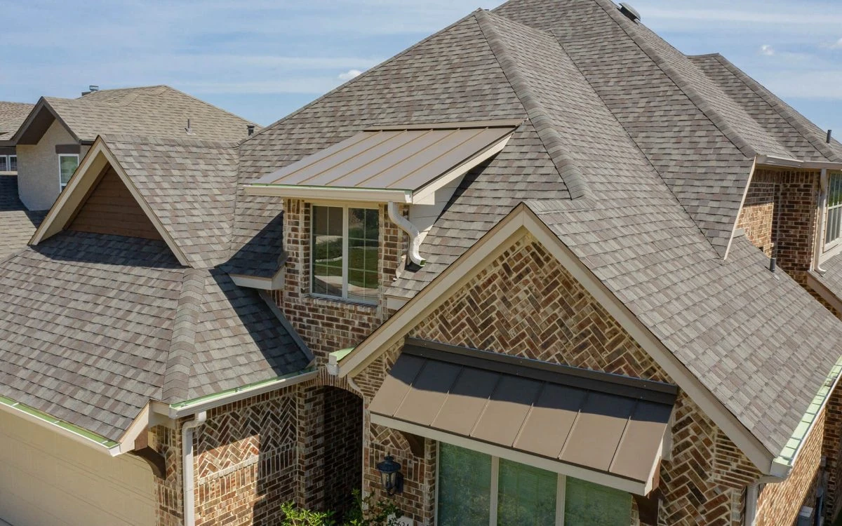 Completed architectural shingle roof with standing seam metal accents on a brick home, installed by Delta Roofing